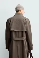 Trench de corte regular confeccionado en tejido técnico italiano repelente al agua. Presenta cuello con solapas de muesca, cierre frontal de botonadura cruzada, cinturón ajustable del mismo tejido, bolsillos de vivo en la cadera, manga larga con puños ajustables y abertura central en la espalda.