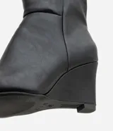 Bota de caña alta Satinato en color negro, confeccionada en material sintético con acabado liso. Presenta un diseño de punta fina y tacón tipo anabela, con una estructura ajustada a la pierna.