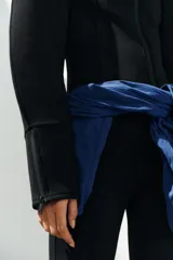 Chaqueta negra de cuello subido con cierre frontal de cremallera termosellada, manga larga con puños anchos y cremalleras laterales en los puños.
