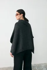 Capita de tejido de punto grueso en color gris oscuro, con cuello alto y diseño holgado tipo poncho.