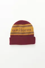 Gorro de lana reversible color borgoña con franjas horizontales color mostaza y la palabra "uniform" en el centro.