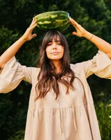 Vestido corto color beige, de lino y corte en A, con escote en V con tiras para anudar y mangas amplias.