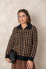 Chaqueta de punto grueso con patrón geométrico de puntos negros sobre fondo marrón, cuello camisero, cierre frontal con cremallera y tirador circular, y bolsillos frontales.