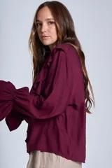 Blusa de color marrón con escote en V, mangas largas abullonadas con puños elásticos y detalles de volados en los hombros y el frente.