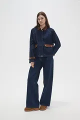 Campera de jean azul oscuro con cuello y puños de pana en color marrón. Presenta cierre frontal, costuras a la vista y detalles de botones metálicos en los puños.