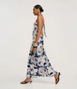 Vestido largo estilo slip con cuello halter que se ata en la nuca, sin mangas, con estampado abstracto en tonos azul y blanco que simula un efecto tie-dye.