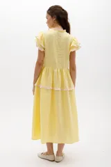 Vestido midi de lino blanco con diseño de broderie, cuello alto, cierre frontal con botones y volados decorativos en los hombros y el cuerpo.