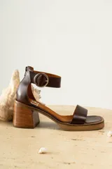 Sandalias de cuero color marrón con tira ancha sobre los dedos y tira con hebilla al tobillo. Tacón de madera.