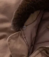 Campera bomber de sarga color tostado con cuello desmontable de pelo sintético oscuro. Presenta cierre frontal de cremallera, puños y cintura acanalados, y bolsillos laterales.