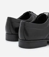 Zapato de vestir negro, confeccionado en cuero sintético, con puntera cuadrada, cierre con cordones y suela de goma.
