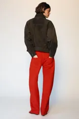 Cazadora tipo bomber de tejido efecto ante color marrón oscuro, con cuello subido, manga larga y cierre frontal con cremallera y botones ocultos. Presenta bolsillos frontales con solapa y botones metálicos.