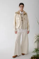 Camisa de cuero metalizado color champagne, con cuello de piel sintética color beige, cierre frontal con botones dorados, bolsillos con solapa en el pecho y corte recto.