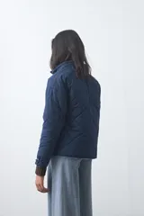 Campera acolchada de nylon color negro, con cuello alto, cierre frontal y botones a presión. Presenta un diseño de rombos y forro interior suave.