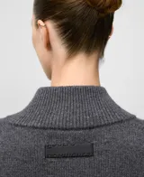 Cárdigan de punto color gris oscuro, confeccionado en lana merino. Presenta cuello alto tipo perkins, manga larga con hombro caído y cierre frontal de botones. Los puños y el ruedo tienen terminación en canalé.