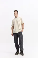 Remera de manga corta color crema con cuello redondo y fit regular. Presenta un estampado grande en la espalda con una flor estilizada en tonos rojo y azul, y texto que incluye "WE ALL GROW" y "trust the process, great things take time".