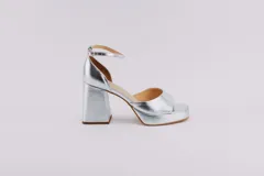 Sandalias plateadas de cuero con plataforma y tacón cuadrado. Tienen pulsera al tobillo con hebilla ajustable.