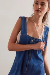 Enterito de denim azul con calce relajado, escote cuadrado, cierre frontal y diseño tipo jardunera con bolsillos.