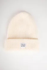 Gorro de lana color crema con etiqueta con logo de la marca Piece of Cake en el dobladillo.