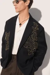 Blazer de corte relajado confeccionada en tejido con lana, color negro. Presenta cuello con solapas de muesca, cierre frontal de un botón y bolsillos de plastrón en la cadera. Destaca por su bordado en hilo dorado con motivos vegetales en la parte frontal.