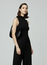 Bolso de hombro negro de efecto cuero, con forma curva y cierre de cremallera. Presenta costuras decorativas en el cuerpo y correa ajustable para llevar al hombro.