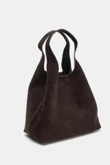 Bolso formato mini shopper confeccionado en piel de ante color topo. Cuenta con doble asa de mano, asa bandolera extraíble, cierre mediante botón imantado y bolsillo interior con cremallera.