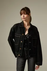 Campera de jean color negro con costuras a contratono, diseño de corte holgado, cuello camisero, cierre frontal con botones metálicos y dos bolsillos frontales con solapa.