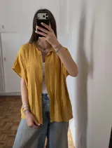 Camisa de muselina color mostaza, de corte oversize, con mangas cortas y cierre frontal de botones.