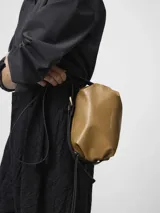 Bolso bandolera pequeño de Adolfo Dominguez con textura craquelada y acabado brillante. Cuenta con un compartimento principal con cierre de cremallera, bolsillo interior con cierre y asa larga regulable en color negro.