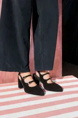 Zapatos de tacón cuadrado con diseño de doble tira con hebillas metálicas doradas sobre el empeine. Presentan punta fina y están confeccionados en cuero gamuzado negro.