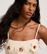 Blusa cropped color crudo, tejida a crochet, con breteles finos y apliques de flores con centro marrón.