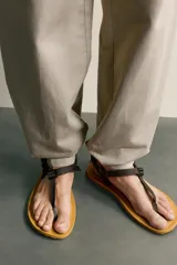 Sandalia multitiras de hombre, con suela plana tostada y tiras de tejido negro con costuras amarillas, ajuste con hebilla plástica y separación para el dedo.