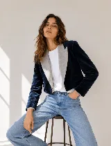 Chaqueta corta de terciopelo azul marino con solapas en contraste de color gris claro. Presenta un diseño estructurado, cierre frontal y bolsillos laterales con solapa.