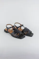 Sandalias de cuero color negro, de suela plana, con tiras entrelazadas en la capellada y tira ajustable en el talón con hebilla metálica.