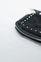 Cartera negra de gamuza con tachas plateadas en el borde inferior y lateral. Tiene una correa de cadena plateada con un detalle de hombrera de gamuza.