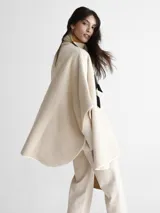 Saco tipo capa color beige con diseño espigado, cuello alto y cierre con un botón.