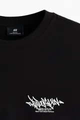 Remera de algodón negra con cuello redondo y diseño de estampado tipográfico en el pecho, corte holgado.