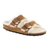 Sandalia Birkenstock modelo Arizona, confeccionada en gamuza color tostado con interior y bordes forrados en piel sintética blanca. Presenta dos correas ajustables con hebillas metálicas y suela de goma oscura.