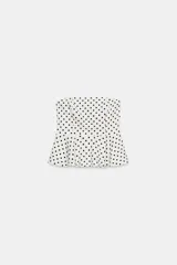 Top palabra de honor de color blanco con estampado de lunares negros, diseño sin tirantes y bajo con volados tipo peplum.