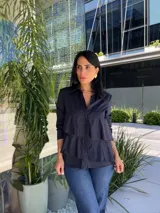 Camisa azul marino de manga larga con cuello camisero y cierre de botones. Presenta volantes horizontales en la parte delantera.