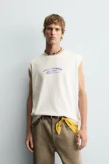 Camiseta tipo tank (sin mangas) de corte relajado, color blanco roto con efecto lavado. Presenta un estampado frontal en azul con texto en francés: "Coquillages Grillés De Côte-Marine" y "Salty Shack".