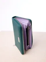 Billetera rectangular de cuero sintético con textura granulada, color bordó. Cuenta con cierre perimetral metálico y placa metálica con el logo de la marca en el frente.