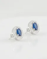 Caravanas de plata 925 con diseño ovalado, piedra central azul tipo zafiro rodeada por un marco de circonias brillantes.