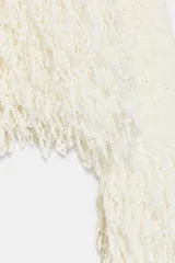 Jersey de punto color blanco crudo, con cuello subido y manga larga. Presenta detalles de flecos en los puños y el dobladillo.