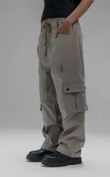 Pantalón cargo de corte oversize y silueta estructurada, confeccionado en microfibra pesada con leve elasticidad. Presenta cintura elástica con cordón de ajuste externo, cierre frontal con botón metálico, bolsillos laterales y bolsillos cargo de gran tamaño con tapa y broches a presión.