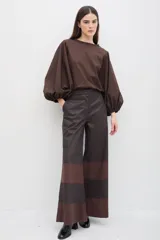 Pantalón de corte amplio y pierna ancha, confeccionado en gabardina de algodón con acabado engomado. Presenta un diseño de paneles horizontales en contraste de colores marrón y negro.
