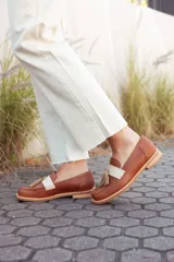 Mocasines de cuero color tostado, con detalle de antifaz en cuero crudo y borlas decorativas. Hechos a mano en Uruguay.