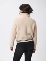 Sweater de tejido grueso en color beige, con cuello alto y cierre frontal parcial. Presenta detalles de rayas negras en contraste en el borde del cuello y en los puños.