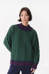 Buzo de tejido de punto con diseño de trenzas, color crema con detalles en marrón en cuello, puños y ruedo. Presenta líneas finas en contraste y pequeñas costuras decorativas en forma de cruz.