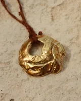 Collar artesanal con dije de flor en bronce o alpaca, suspendido en un cordón de seda natural teñido a mano. El diseño permite atarse con un moño, ofreciendo versatilidad para lucirlo de distintas formas.