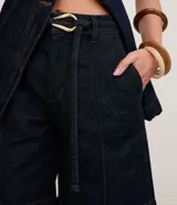 Bermuda de jeans azul oscuro, tiro medio, con costuras contrastantes y cinturón de lazo de tela con hebilla metálica de forma irregular.